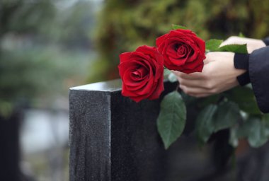 Siyah granit mezar taşının yanında kırmızı gülleri olan bir kadın.