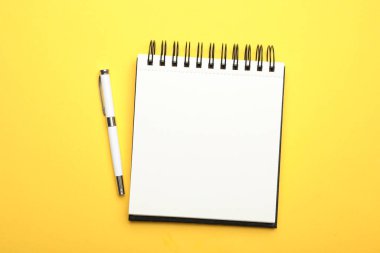 Sarı arkaplan üzerinde açık defter ve kalem, üst görünüm