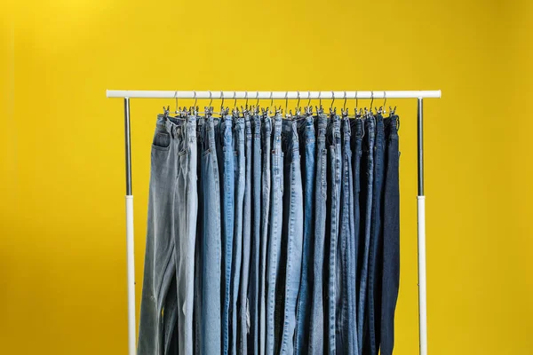 Rack med olika jeans på gul bakgrund — Stockfoto
