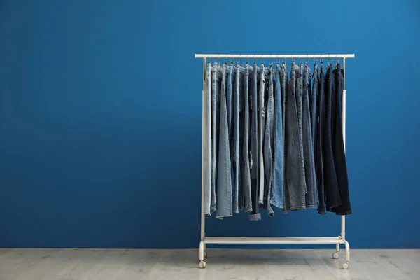 Scaffale con jeans alla moda vicino al muro blu. Spazio per testo — Foto Stock
