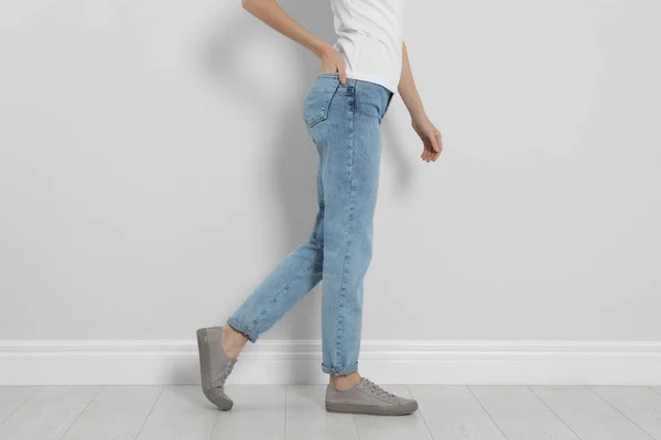 Jonge vrouw in stijlvolle jeans bij lichte wand, close-up — Stockfoto