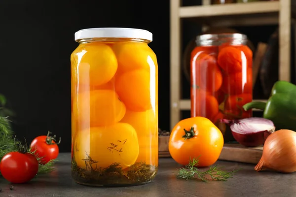 Skleněné nádoby s nakládanými rajčaty na šedém stole — Stock fotografie