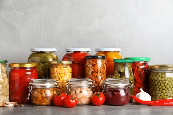 Pots en verre avec différents légumes marinés sur table grise — Photo