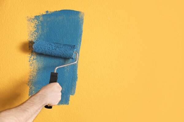 Man painting yellow wall with blue dye, closeup. Space for text