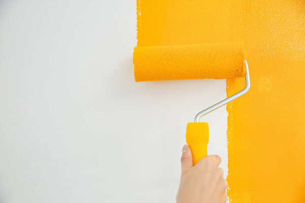 Woman painting white wall with yellow dye, closeup. Interior renovation