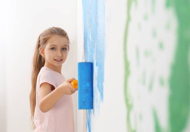 Küçük çocuk evin içinde fırçayla duvar boyuyor.