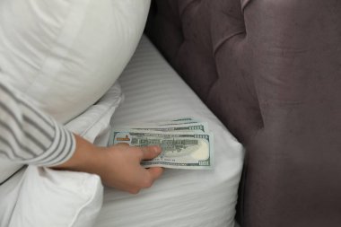 Yatak odasındaki yastığın altına para saklayan kadın, yakın plan. Para tasarrufu
