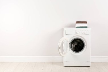 Beyaz duvarın yanında havlu yığını olan modern çamaşır makinesi.
