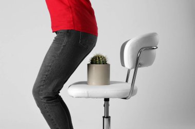 Woman sitting down on chair with cactus against white background, closeup. Hemorrhoids concept clipart