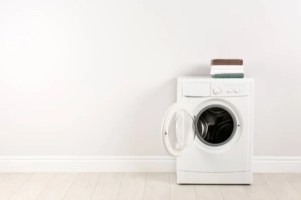 Modern mosógép halom törölköző közelében fehér fal, spa — Stock Fotó