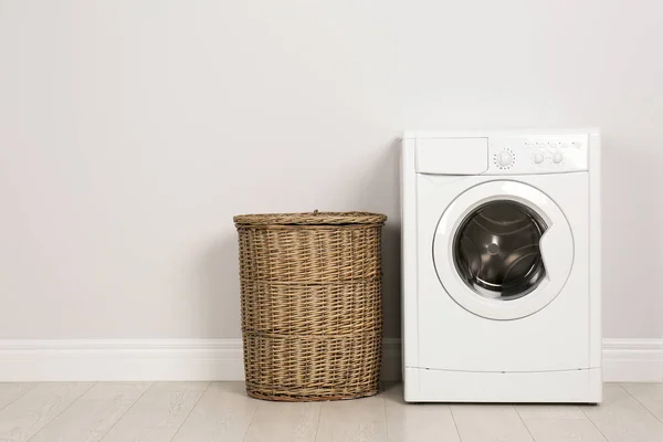 Modern washing machine with laundry basket near white wall — 스톡 사진