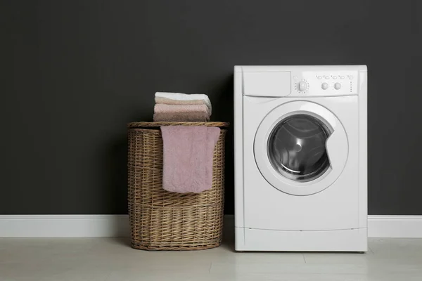 Современная стиральная машина и корзина для белья возле черной стены — стоковое фото