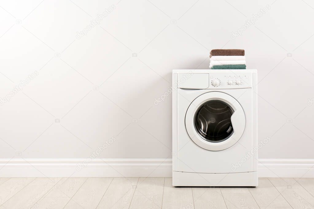 Modern washing machine with stack of towels near white wall, spa