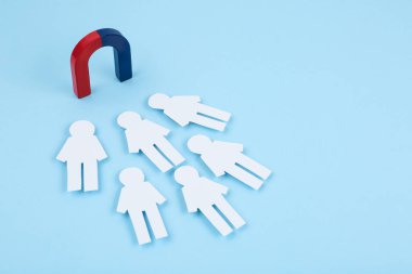 Magnet attracting paper people on light blue background clipart