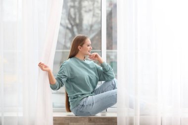 Güzel genç kadın evde pencereden dışarı bakıyor