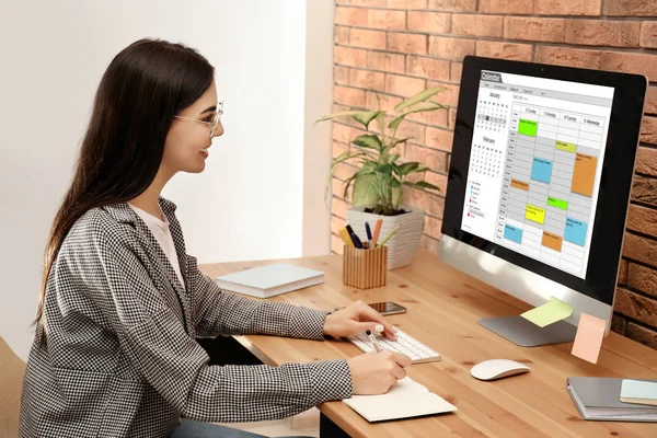 Mujer joven utilizando la aplicación de calendario en el ordenador en la oficina —  Fotos de Stock