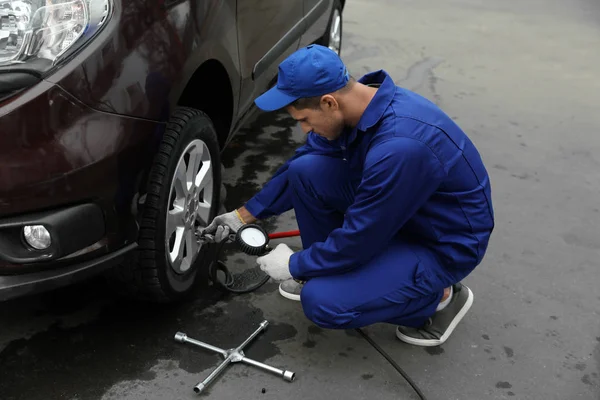 Trabajador verificando la presión del neumático en la rueda del coche en la estación de servicio — Foto de Stock