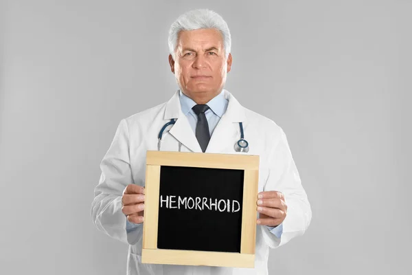 Doctor Sosteniendo Pizarra Con Palabra Hemorrhoid Sobre Fondo Gris Claro — Foto de Stock