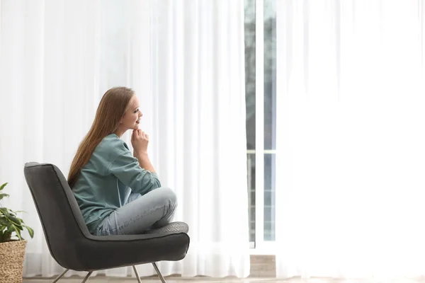 Mujer joven sentada en sillón cerca de la ventana en casa — Foto de Stock