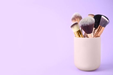 Eflatun arkaplanda bulunan profesyonel makyaj fırçaları