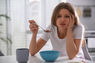 Uykulu genç kadın sabah kahvaltısını evde yiyor.