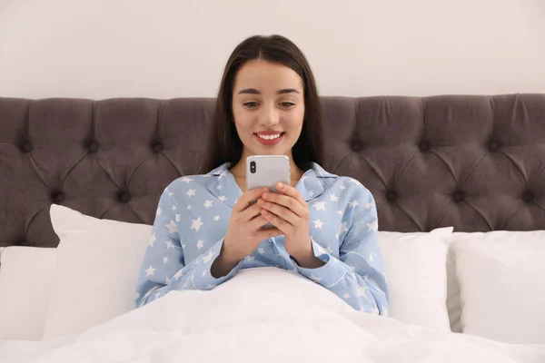 年轻女人在家里的床上沉溺于智能手机 — 图库照片