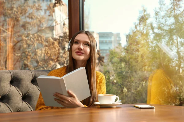 Mujer escuchando audiolibro en la mesa en la cafetería — Foto de Stock