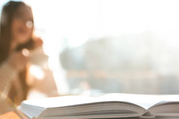 Book on table in cafe and woman with headphones on background. A