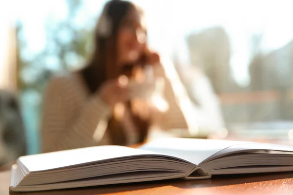 Libro en la mesa en la cafetería y la mujer con auriculares en el fondo. A — Foto de Stock