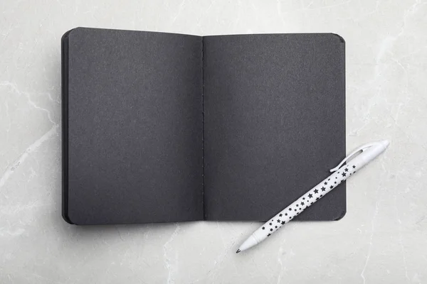 Elegante notebook nero aperto e penna sul tavolo in marmo, vista dall'alto — Foto Stock