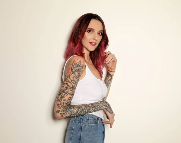 Beautiful woman with tattoos on arms against light background