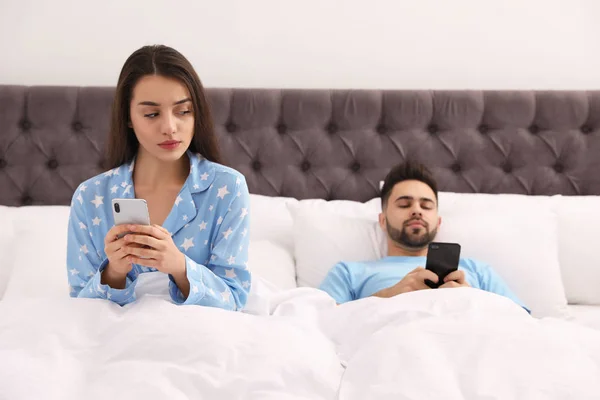 Pareja joven con smartphones en la cama en casa — Foto de Stock