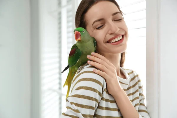 Young woman with cute Alexandrine parakeet indoors — 스톡 사진