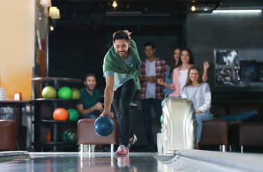 Genç adam top oynuyor ve arkadaşlarıyla bowling kulübünde vakit geçiriyor.
