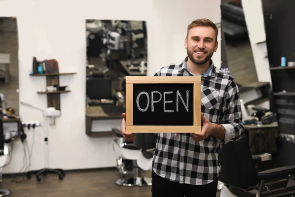 Young business owner holding OPEN sign in his barber shop