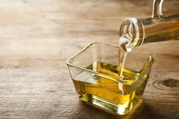 Pouring cooking oil from jug into bowl on wooden table