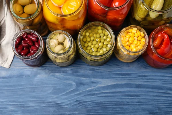 Glass jars with different pickled vegetables on blue wooden tabl — 스톡 사진