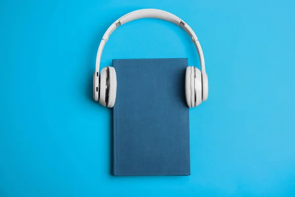 Libro y auriculares modernos sobre fondo azul claro, vista superior —  Fotos de Stock