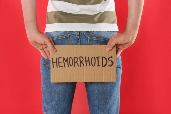 Man holding carton sign with word HEMORRHOIDS on red background, closeup