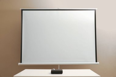 Video projector and screen near beige wall indoors. Space for design clipart