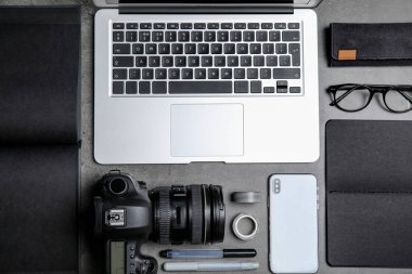 Gri taş masanın üzerinde dizüstü bilgisayarı, kamerası ve akıllı telefonu olan düz bir kompozisyon vardı. Tasarımcının işyeri