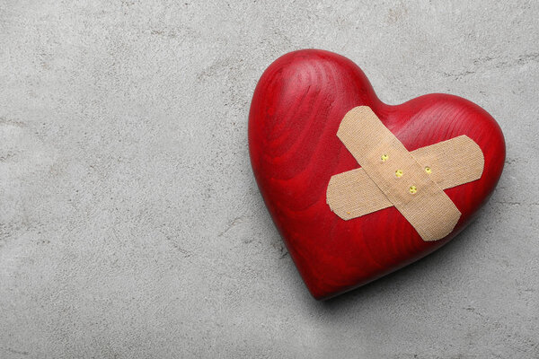 Red wooden heart with sticking plasters on light grey stone table, top view. Space for text