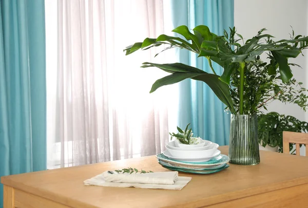 Vaatwerk en planten op houten tafel in de buurt van venster met elegante cur — Stockfoto