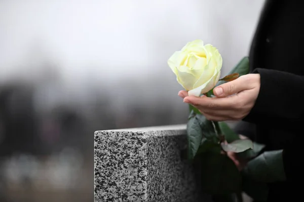 Mulher segurando rosa branca perto de granito cinza lápide ao ar livre, c — Fotografia de Stock