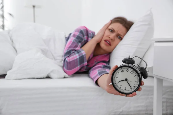 Mujer joven emocional con despertador en casa por la mañana, enfoque — Foto de Stock