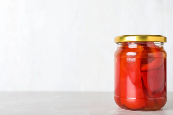 Glass jar of pickled red bell peppers on light marble table. Spa — 스톡 사진