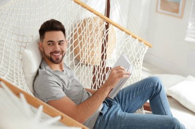 Genç adam evde hamakta kitap okuyor.