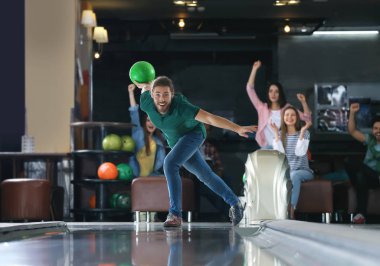 Genç adam top oynuyor ve arkadaşlarıyla bowling kulübünde vakit geçiriyor.