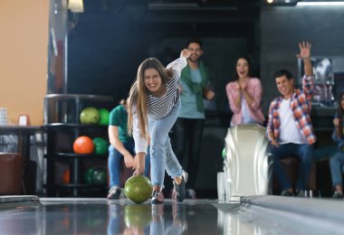 Genç bir kadın top oynuyor ve arkadaşlarıyla bowling kulübünde vakit geçiriyor.
