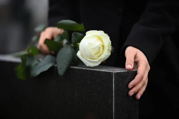 Woman holding white rose near black granite tombstone outdoors, — 스톡 사진